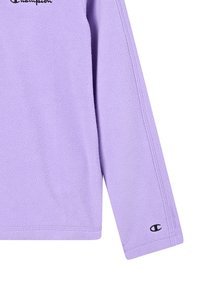 Haut à manches longues en polaire lilas avec un logo "Champion" brodé en noir près du col et un petit logo "C" sur la manche inférieure.