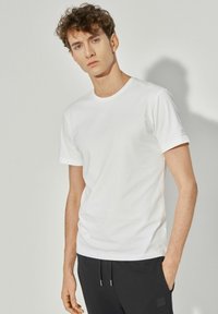 Biała koszulka z krótkim rękawem z bawełny, z okrągłym dekoltem i subtelnym logo na rękawie, w komplecie z czarnymi spodniami na sznurek.