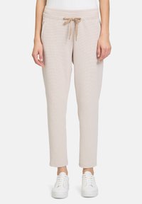 Beige gewebte Jogginghosen mit elastischem Taillenbund, Kordelzugdetails, Seitentaschen und schmal zulaufenden Bündchen, kombiniert mit weißen Sneakers.