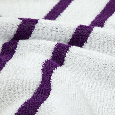 Serviette blanche à surface texturée, avec deux bandes violettes horizontales. Le tissu semble doux et absorbant.