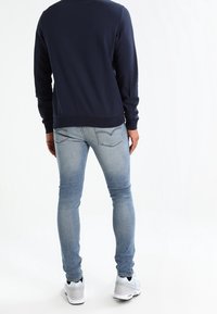Námořnická mikina s dlouhými rukávy, žebrovanými manžetami a lemem, doplněná světle modrými skinny džíny se sepraným vzhledem a zadními kapsami.