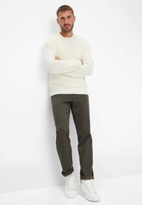 Maglione dalla texture cremosa, pantaloni verde oliva e sneakers bianche. Il maglione ha un collo a girocollo e polsini a coste; i pantaloni hanno una vestibilità casual.