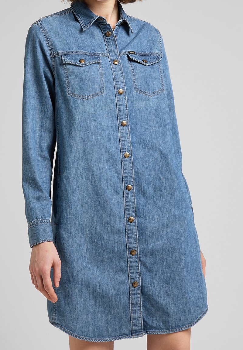 Denimskjortklänning med krage, långa ärmar, knäppning fram med knappar och två bröstfickor. Ljusblå färg med slitna detaljer.