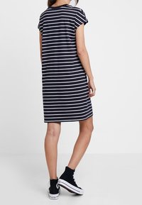 Randig t-shirtklänning med korta ärmar, marinblå och vita ränder. Mjuk tyg, rak modell, bärs med svarta högskoor.