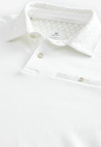 Weißes Poloshirt mit strukturiertem Kragen, zwei Knöpfen, TaschenDETAILS und einem gemusterten Innenfutter. Aus glattem Stoff gefertigt. Reguläre Passform.