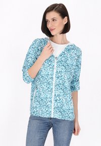 Jachetă ușoară în nuanță de verde teal, cu un model floral, închidere tip fermoar și glugă. Prezintă mâneci elasticizate și o textură a țesăturii moale.