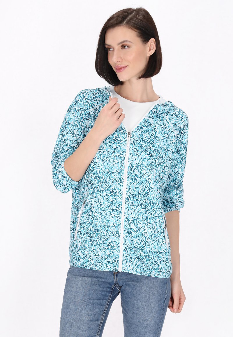 Jachetă ușoară în nuanță de verde teal, cu un model floral, închidere tip fermoar și glugă. Prezintă mâneci elasticizate și o textură a țesăturii moale.