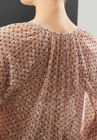 Haut en tissu pêche transparent avec des pois noirs, présentant de délicats motifs floraux. Design plié au dos et encolure arrondie.