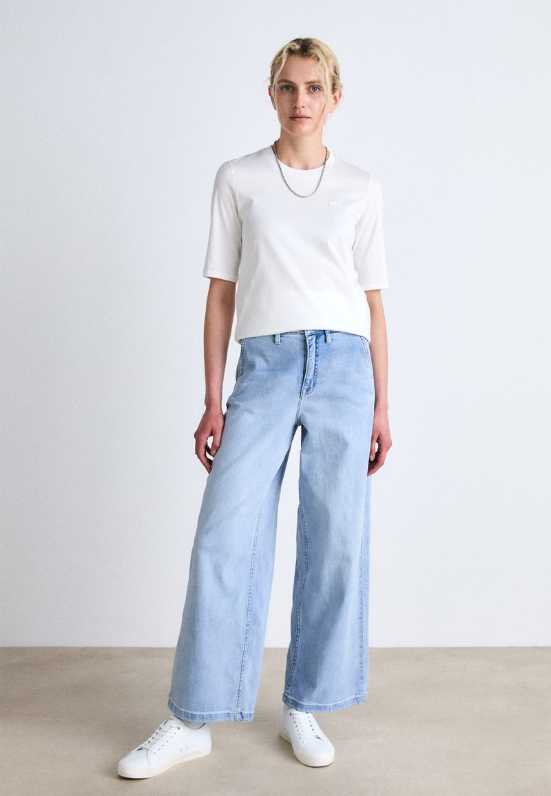 Biała bluzka z krótkim rękawem, jasnoniebieskie szerokie dżinsy i białe sneakersy. Gładki materiał, luźny krój, minimalistyczny design, bez widocznych wzorów.