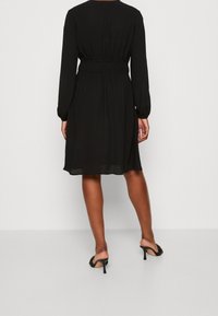 Schwarzes langärmliges Kleid mit gerafftem Bund, knielangem Schnitt, fließendem Stoff und glatter Textur. Schlichtes und klassisches Design.
