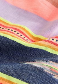 Nærbillede af farverigt vævet stof med vandrette striber i pastel lilla, fersken, neongul, orange, rød og marineblå.