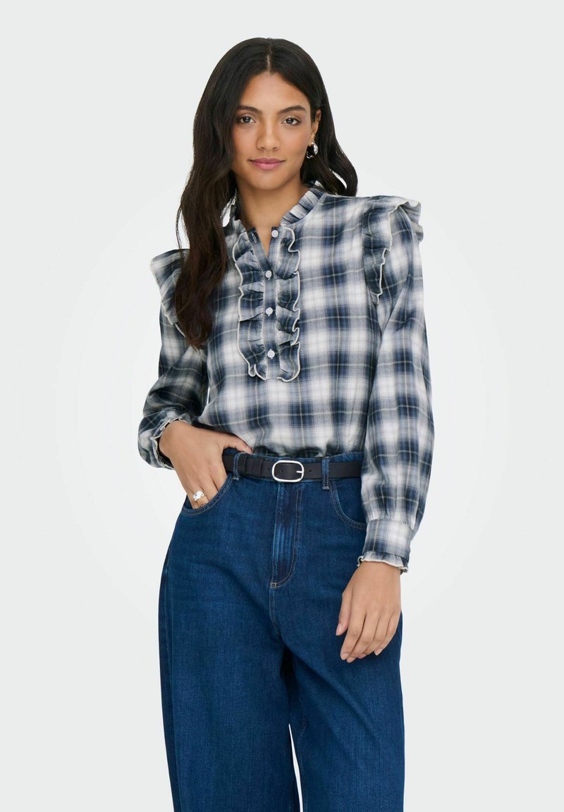 Blå og hvid ternet skjorte med flæser på skuldrene og knappet foran. Sammen med højtaljede mørkeblå jeans og et sort bælte.