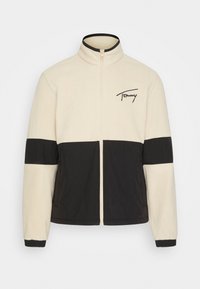 Fleecepaita, jossa on kermahtava runko mustin yksityiskohdin, vetoketjullinen suljenta, korkea kaulus ja rintataskussa kirjailtu logo.