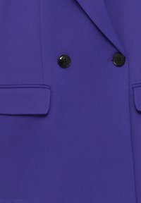Veste violet satinée à double boutonnage, avec deux boutons noirs et des revers structurés. Comprend deux poches latérales.