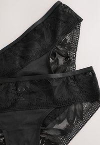 Deux pièces de lingerie noire en dentelle avec des motifs floraux posées en chevauchement sur une surface claire.