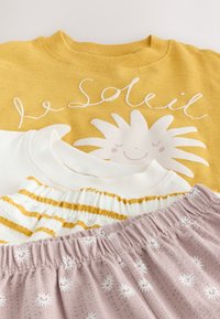 Žluté tričko s grafikou slunce a textem "le soleil", bílo-žlutá pruhovaná látka a světle fialová látka s bílými květinovými potisky.