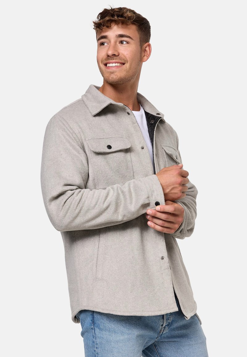 Giacca grigio chiaro in misto lana con chiusura frontale a bottoni, due tasche sul petto e maniche lunghe. Presenta un colletto classico e una texture liscia.