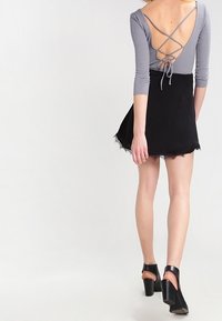 Šedé tričko s dlouhým rukávem a nízkým zkříženým zády, kombinované s černou minisukní s krajkovým lemem a černými sandály na podpatku s páskem kolem kotníku.