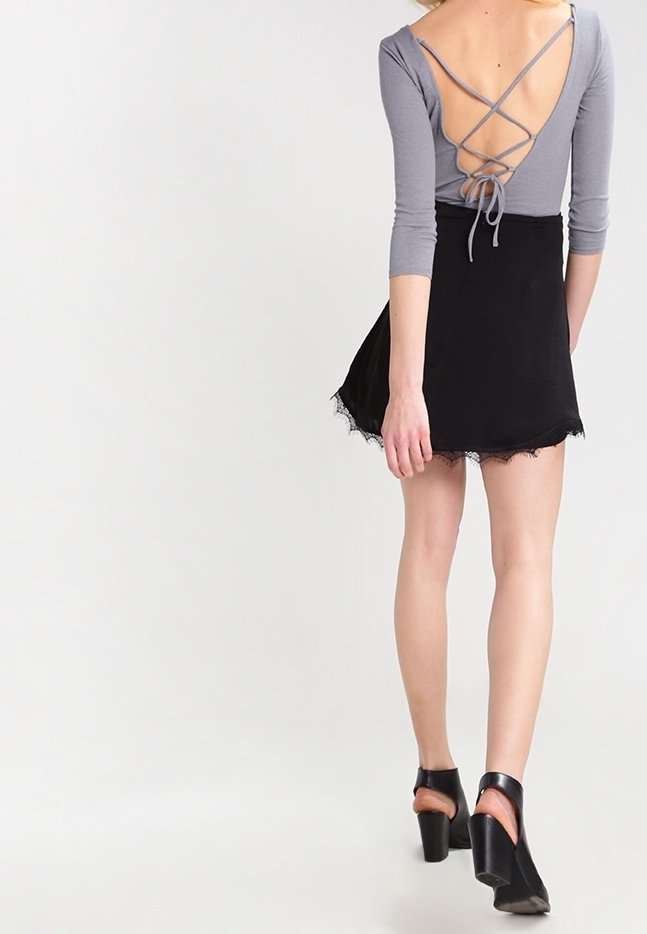 Šedé tričko s dlouhým rukávem a nízkým zkříženým zády, kombinované s černou minisukní s krajkovým lemem a černými sandály na podpatku s páskem kolem kotníku.