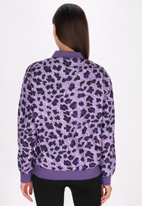 Giacca bomber viola con motivo astratto nero e lavanda, maniche e orlo a costine. Realizzata in tessuto leggero e morbido.