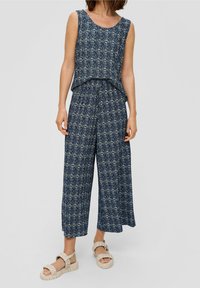 Ensemble deux pièces bleu marine à motifs, composé d'un haut sans manches et d'un pantalon à jambes larges, avec des accents crème subtils et une coupe décontractée. Porté avec des sandales beige.