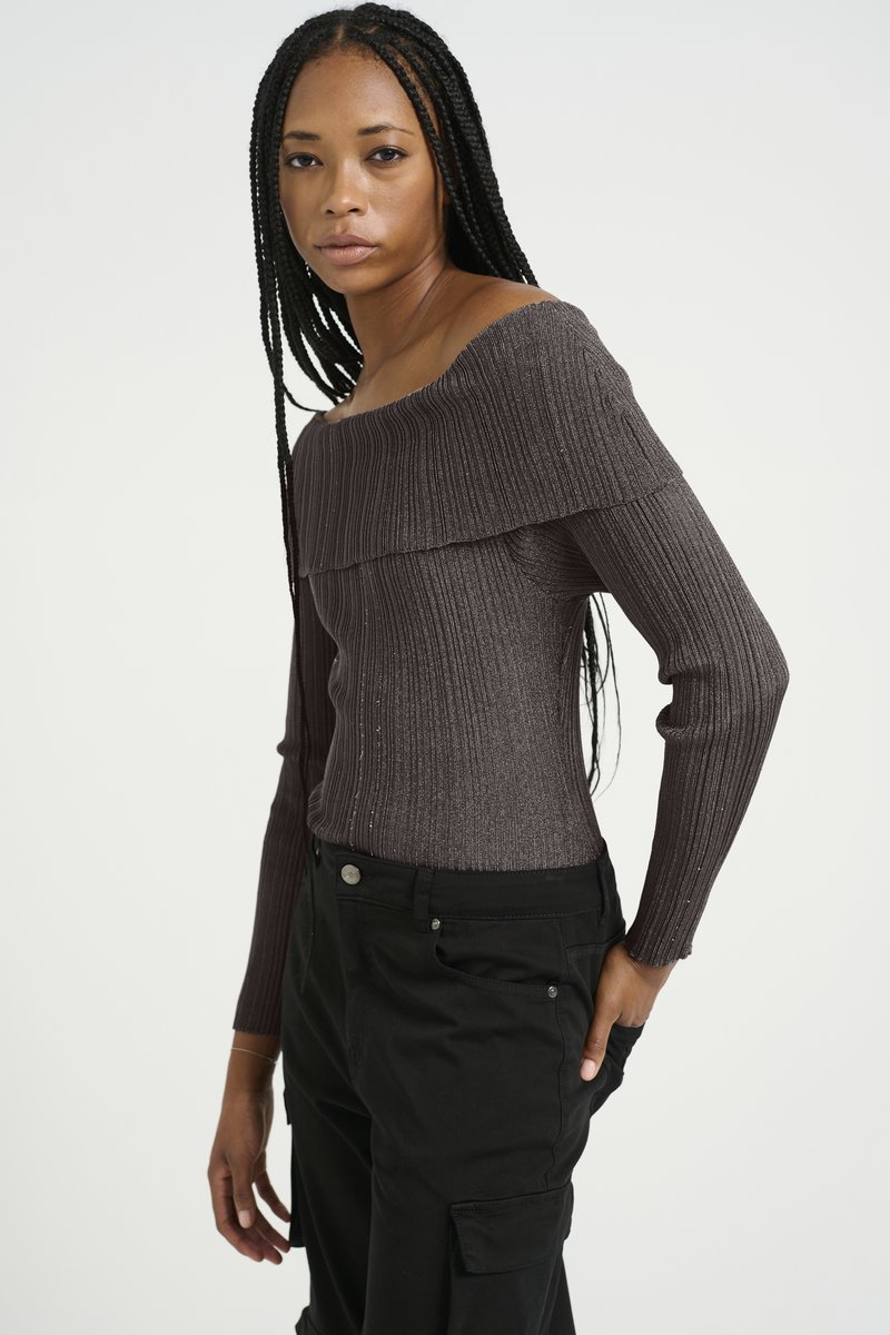 Dunkelgrauer, schulterfreier, gerippter Pullover mit langen Ärmeln, der eine strukturierte Oberfläche aufweist. Kombiniert mit schwarzen Cargo-Hosen, die eine schlanke Silhouette betonen.