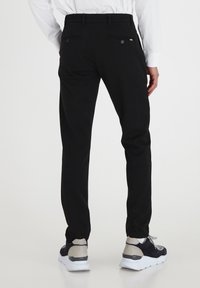 Črne hlače slim fit z dvema zadnjima žepoma s gumbom in gladko teksturo. Ugotovljene z sivo-navy supergami.