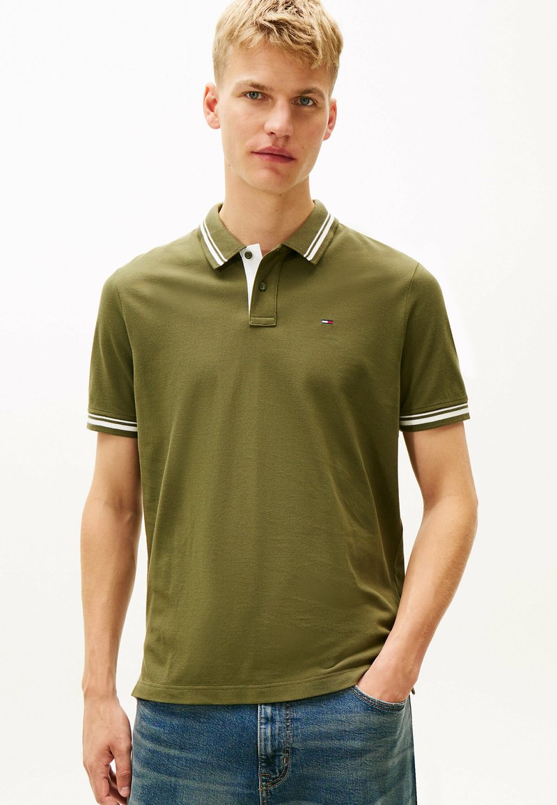 Oliwkowa koszulka polo z białym i granatowym paskowanym kołnierzykiem. Krótkie rękawy, strukturalna tkanina i małe logo na lewej piersi. Casualowy krój.
