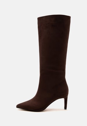 Botte haute en daim marron foncé pour femme, avec bout pointu et talon fin de hauteur moyenne sur fond blanc.
