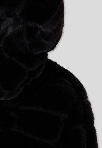 Felpa con cappuccio in pelliccia sintetica nera che presenta una texture soffice, un cappuccio arrotondato e un tessuto morbido. La vista ravvicinata evidenzia la lucentezza e le fibre dense.