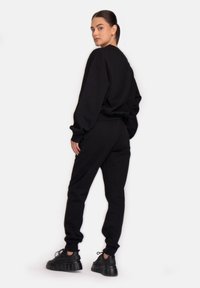 Melns sporta krekls un atbilstošas bikses brīvā piegriezumā. Gluda tekstūra, apaļa kakla izgriezuma forma un elastīgas aproces. Valkā ar masīviem melniem sporta apaviem.