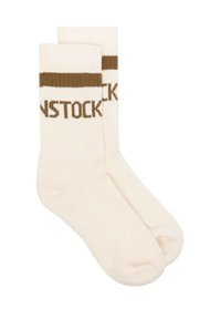 Calcetines beige con puños acanalados marrones y texto tejido que dice "BIRKENSTOCK." Textura suave, longitud a media pantorrilla, diseño casual.