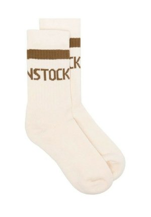 Calcetines beige con puños acanalados marrones y texto tejido que dice "BIRKENSTOCK." Textura suave, longitud a media pantorrilla, diseño casual.