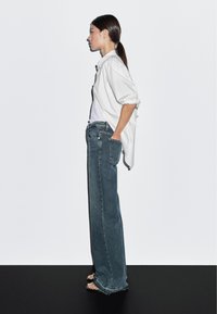 Džíny s širokými nohavicemi v bledě modré barvě, s vysokým pasem a třepenými lemy. V kombinaci s bílou košili s dlouhým rukávem.