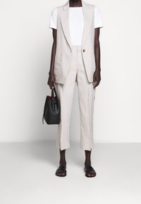 Ljusbeige skräddarsydd väst med stora fickor, i kombination med matchande avsmalnande byxor. Vit, figurnära t-shirt under, svart bucket bag och platta sandaler.