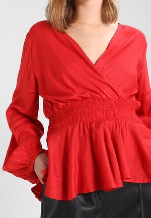 Rød bluse med lange ærmer, smocket talje og flæsekant. Lavet af letvægtsstof, med en dyb V-halsudskæring.