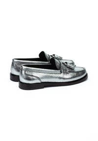 Mocasines plateados metálicos con un acabado texturizado, que presentan un detalle de borlas, una puntera redondeada y una suela de goma negra.