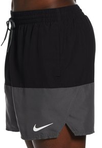 Costumi da bagno Nike neri e grigi con vita elasticizzata, tasche laterali e un logo bianco sul lato sinistro in basso.