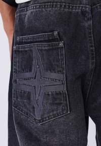 Pantaloni in denim neri con un grande design a stella ricamata sulla tasca posteriore, cuciture a contrasto e due tasche aggiuntive più piccole.