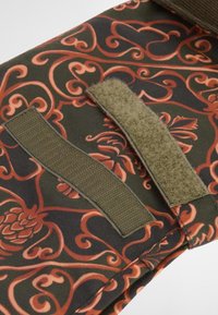 Ύφασμα με περίπλοκο λουλουδάτο σχέδιο σε κόκκινο και πορτοκαλί χρώμα σε σκούρο πράσινο φόντο. Διαθέτει δύο λωρίδες Velcro σε ελαιοπράσινο χρώμα.