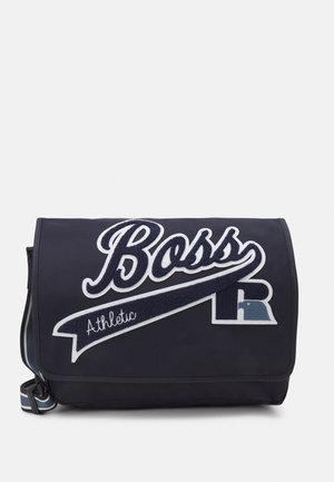 Sac messager bleu marine avec logo « Boss Athletic » blanc et bleu marine et bandoulière rayée réglable sur fond uni.