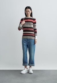 Strikket sweater med horisontale striber i rød, brun og beige, kombineret med opkrogede blå denimjeans og hvide sneakers.