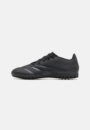 Chaussure de football noire basse avec semelle texturée, lacets et détails subtils de rayures sur fond blanc uni.