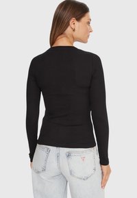 Top nero a maniche lunghe a coste con scollo arrotondato, abbinato a jeans azzurri a vita alta con etichetta logo sulla tasca posteriore.