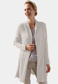 Witte gebreide cardigan met een gestructureerd ontwerp, open voorkant en lange mouwen. Draag het over een top met bloemenprint, gemaakt van een zachte, lichte stof.
