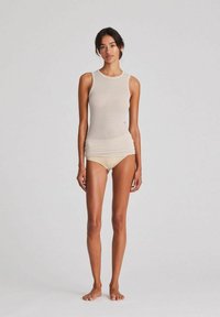 Beige singlet ümmarguse kaelusega, pehme puuvilla seguga kanga, koos sobivate sauma vaba aluspükstega. Mudel seisab paljajalu lihtsa taustaga.