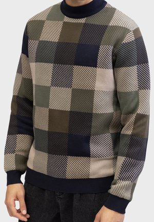 Man wearing a long-sleeve knit sweater with a navy, olive, brown, and beige checkered pattern and ribbed cuffs and neckline.