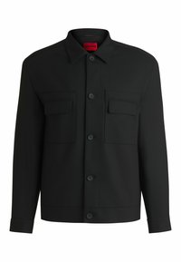 Giacca nera con colletto a punta, chiusura frontale con bottoni e due tasche sul petto. Realizzata in tessuto liscio con una forma strutturata.