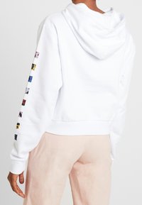 Sudadera blanca recortada con capucha ajustable y acentos de colores en forma de cuadrado a lo largo de los puños de las mangas. Material suave, con dobladillo y puños acanalados.