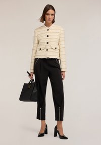 Kermansävyinen tweed-takki mustine nuppeineen ja teksturoituine raitoineen, yhdistettynä mustiin lyhyisiin housuihin, joissa on vetoketjuyksityiskohtia, sekä mustiin korkokenkiin.